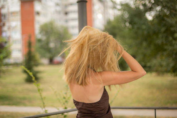 A young attractive female with strawberry blonde hair has her arms crossed as she leans into a strong wind which is blowing her hair completely to the side - isolated on a blue background. Canon 5D MarkII.