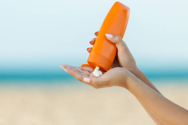 mano de mujer aplicar protector solar en la playa - aplicar fotografías e imágenes de stock