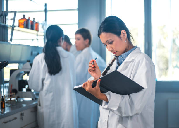 istock Female scientist writing in diary with team in lab 1047801718