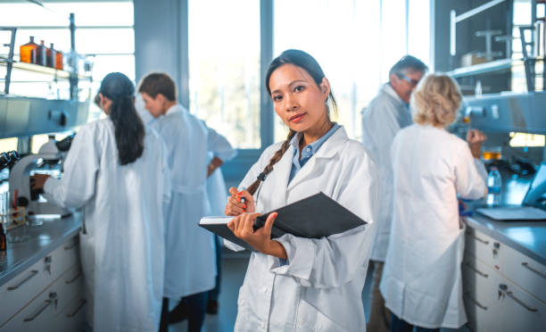 femme scientifique écrit dans le journal avec l’équipe en laboratoire - scientist male young adult doctor photos et images de collection