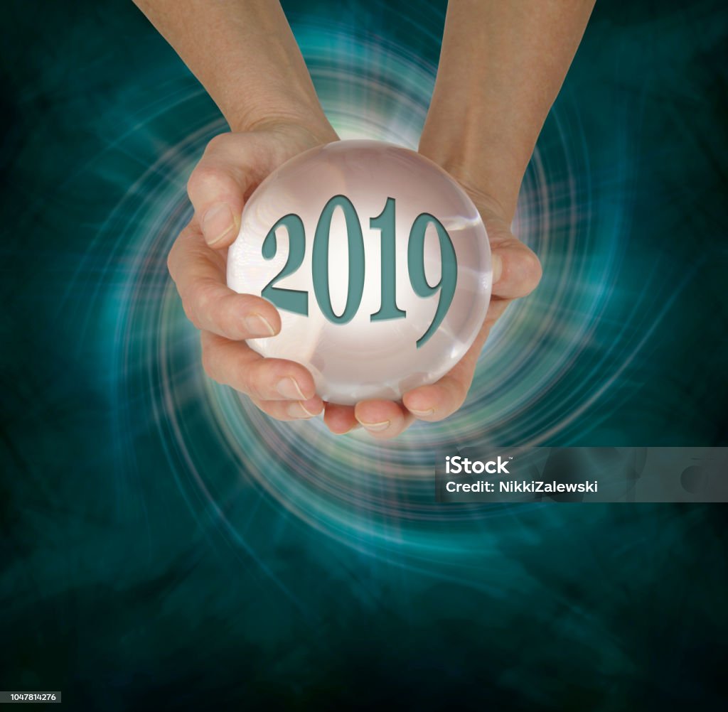 Take a look at what 2019 holds with a Crystal Ball Reading female hands holding a large scrying ball containing the year 2019 against a deep green vortex spiral and copy space  below 2019 Stock Photo