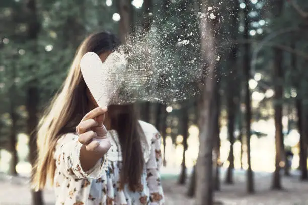 Conceptual female portrait with a broken heart. Holding white heart shape with pixel explosion effect