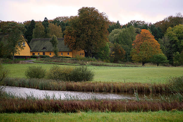Idyllic farm house in an autumn forest with a small lake in front.