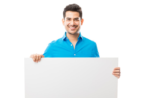Portrait of attractive male smiling while holding blank poster against plain white background