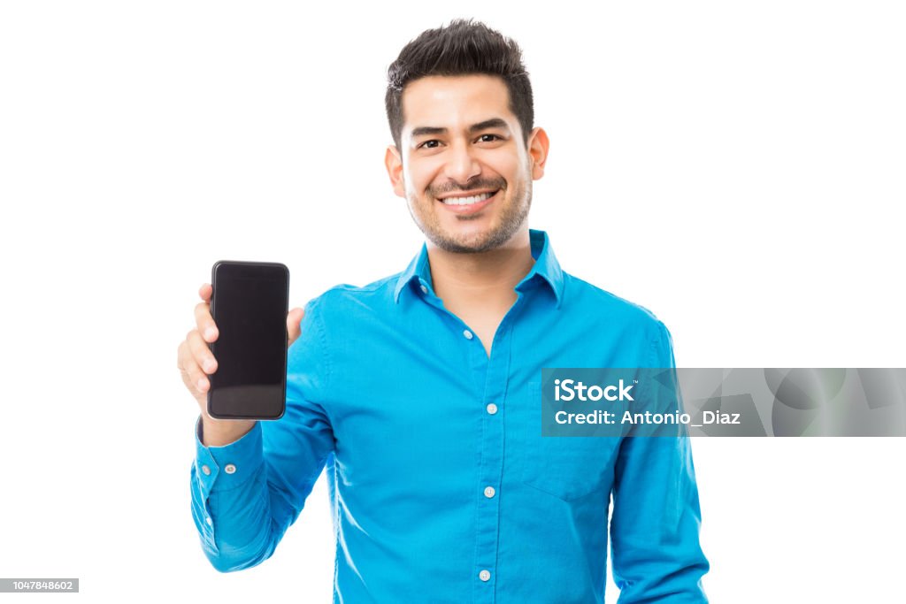 Attractive Male Smiling While Holding Smartphone Portrait of attractive male smiling while holding smartphone against white background Men Stock Photo