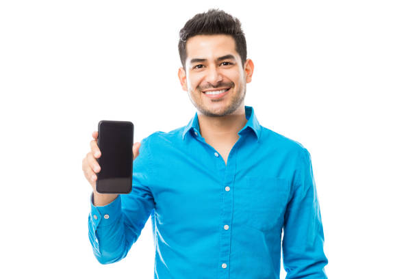 Attractive Male Smiling While Holding Smartphone Portrait of attractive male smiling while holding smartphone against white background how to sell my photography online stock pictures, royalty-free photos & images