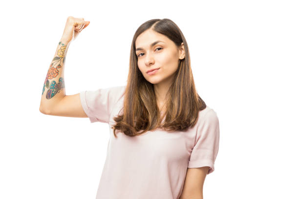 Confident Young Woman Flexing Her Biceps Confident young woman flexing her biceps against white background tattoo arm stock pictures, royalty-free photos & images