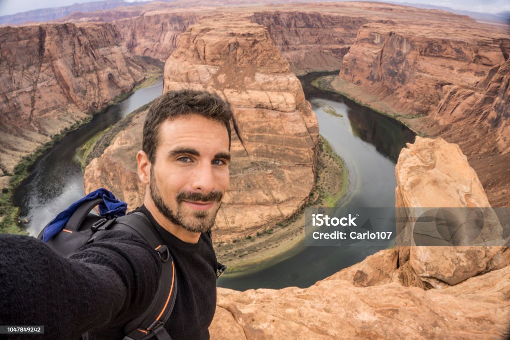 Young adult man taking a selfie at the Horseshoe Bend A young happy traveler taking a selfie. Horseshoe Bend on the Background. Page, Arizona Selfie Stock Photo