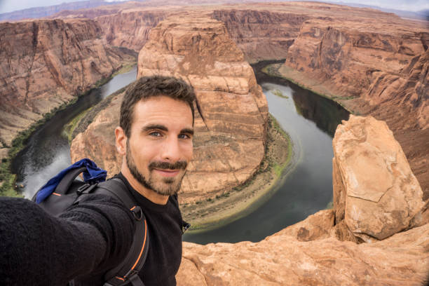 Young adult man taking a selfie at the Horseshoe Bend A young happy traveler taking a selfie. Horseshoe Bend on the Background. Page, Arizona horseshoe bend river stock pictures, royalty-free photos & images