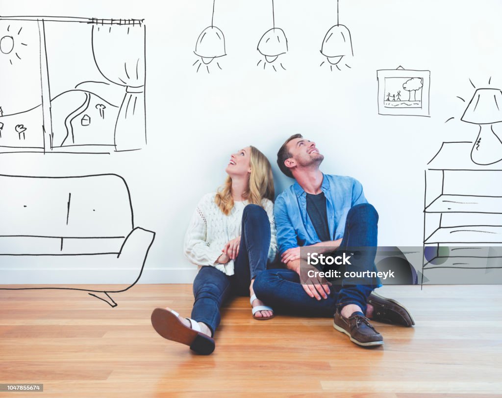 Couple dreaming of their new house. Couple dreaming of their new house. They are sitting on a wooden floor imagining their new home with furniture in it. The house is currently empty. They are booth looking up and smiling happily. Moving House Stock Photo