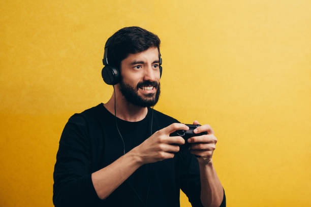 istock Young man playing video game over yellow background 1047871802