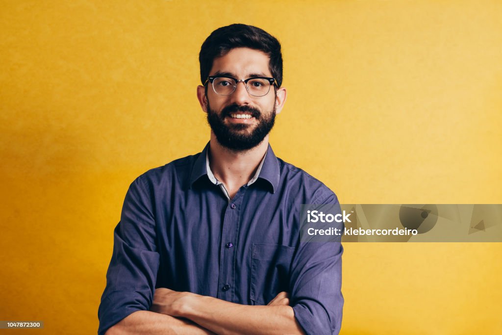 Portrait of a smiling bearded man in eyeglasses looking at camera isolated over yellow background Men Stock Photo