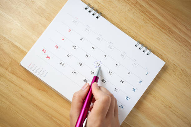 istock calendar page on table with female hand holding pen, top view 1047876232