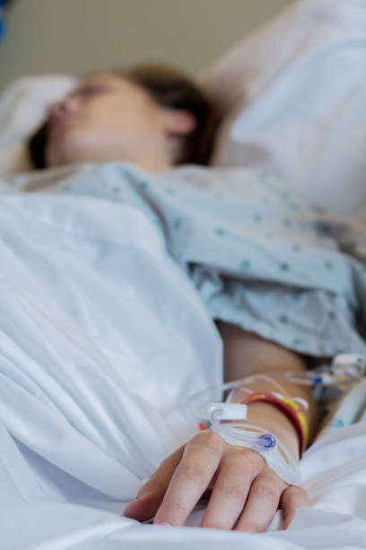 Close up of woman's hand with IV and hospital bracelets during childbirth Young Caucasian woman is lying in hospital bed while preparing to give birth. Photo shows close up of IV in woman's hand with hospital bracelets. sick woman hospital bed stock pictures, royalty-free photos & images