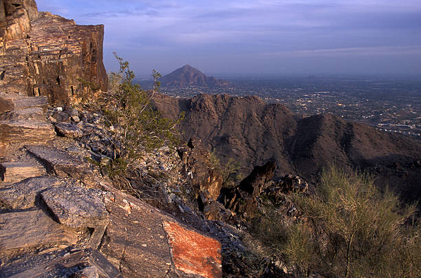 Phoenix Mountain View A rocky outcrop is lit by the evening sun on Squaw Peak in Phoenix, Arizona, with a view of distant mountains and the city. outcrop stock pictures, royalty-free photos & images