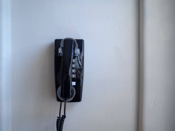 istock Black landline phone and receiver hanging on white wall 1047974066