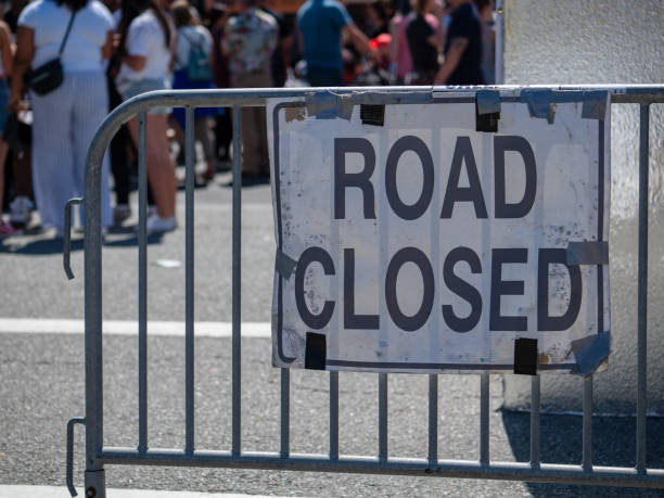 istock Make shift road closed sign hanging on barrier with crowd in back 1047980770