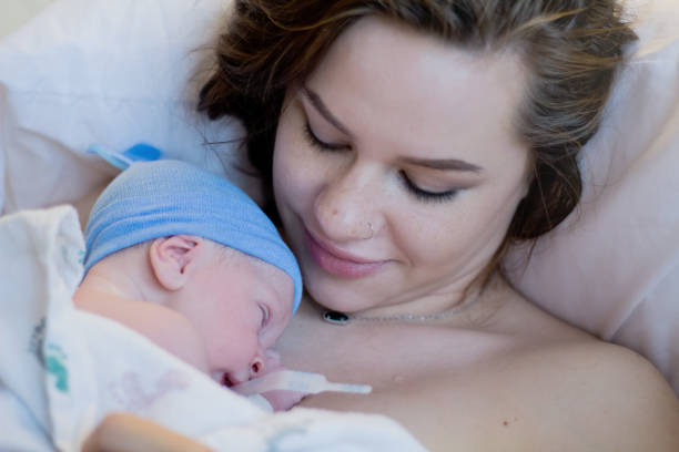 Mother stares lovingly at newborn baby in hospital Newborn baby lays on teenage mother's chest moments after being born. Mother stares lovingly at son while laying in hospital bed. labor childbirth photos stock pictures, royalty-free photos & images