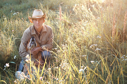 young man in cowboy style and his dog resting in the field toned image
