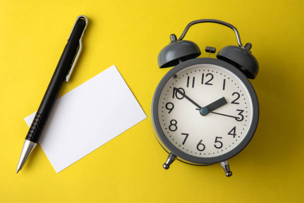 istock Time concept with blank white paper note copy space to add wording or message , a alarm clock with black pen decoration on yellow background 1047995616