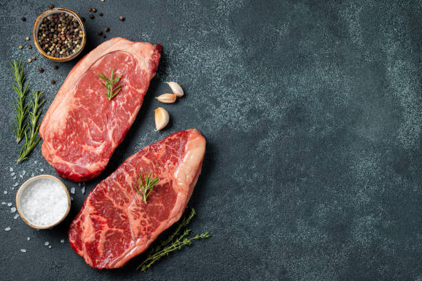 istock Fresh raw Prime Black Angus beef steaks on stone board: Striploin, Rib Eye. Top view with copy space. On a dark background 1048000200