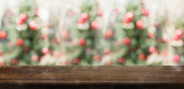Empty rustic wood table top with abstract blur christmas tree red decor ball and snow fall background with bokeh light,winter Holiday backdrop,Mock up banner for display of product or promotion.