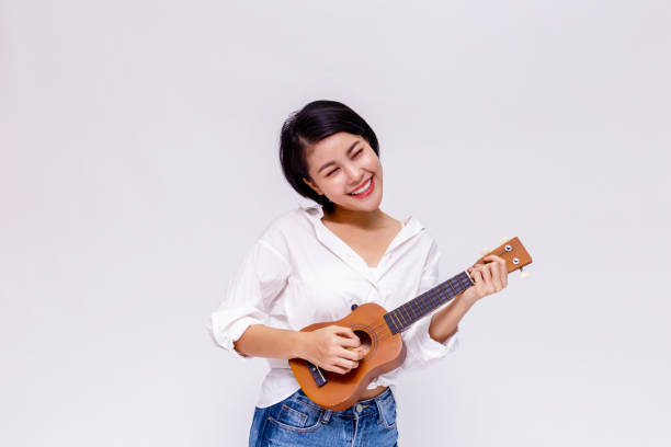 若いアジアの女性の女の子は孤立した白地でウクレレ ビーチ ギターを演奏します。 - ukelele ストックフォトと画像