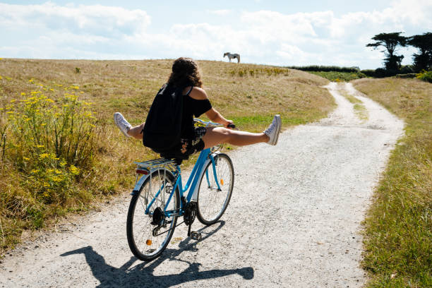 Pretty young woman riding bicycle in a country road Pretty young woman riding bicycle in a country road with her legs in the air brittany france stock pictures, royalty-free photos & images