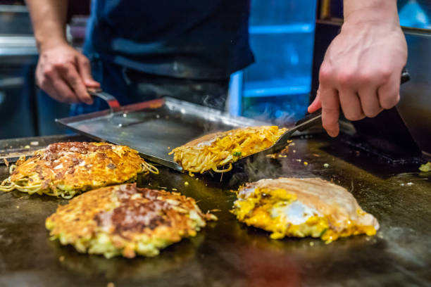 chef is cooking Okonomiyaki chef is cooking Okonomiyaki on the iron plate, he is using the spatula to put the food on to the plate which is already done osaka city photos stock pictures, royalty-free photos & images