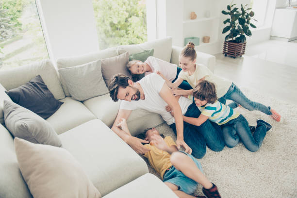 concetto pre-adolescenziale spensierato, spensierato, sognante. angolo alto sopra la vista dall'alto foto di papà barbuto brunet scherzare con quattro bambini vicino a un accogliente divano in interni moderni e leggeri - carpet caucasian domestic room home interior foto e immagini stock