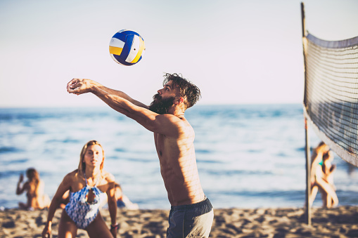 Young man catching the ball while playing volleyball with his friends during summer day on the beach.