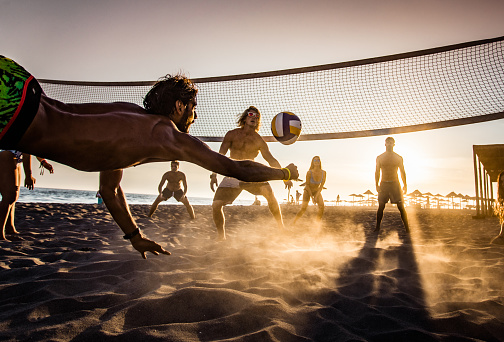 Group of young people having fun while playing beach volleyball in summer day at sunset.