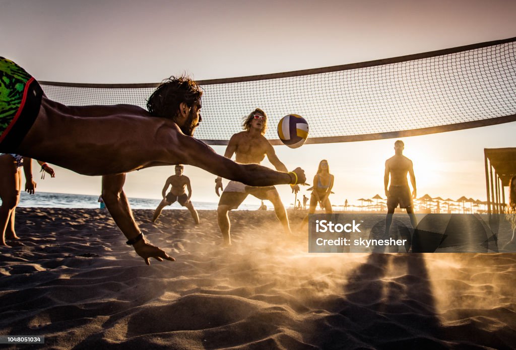 Beach volleyball at sunset! Group of young people having fun while playing beach volleyball in summer day at sunset. Beach Volleyball Stock Photo