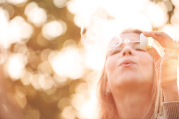 Mid adult Caucasian woman blowing soap bubbles outdoors.