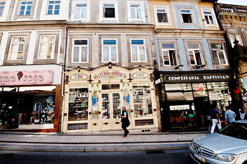 Window Shoppers And Tourists Outside The Popular Cha A Perola do Bolhao Café And Confeitaria Baptista In Porto - Portugal. Mercedes Benz Car Drive By
