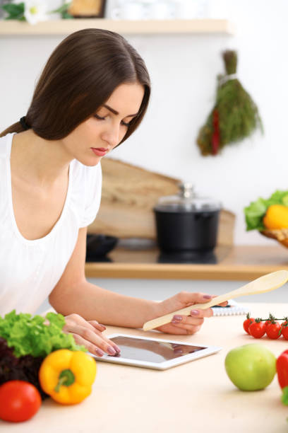 istock Beautiful Hispanic woman cooking while using tablet computer in kitchen. Housewife found new recipe for dinner or breakfast. 1048060376