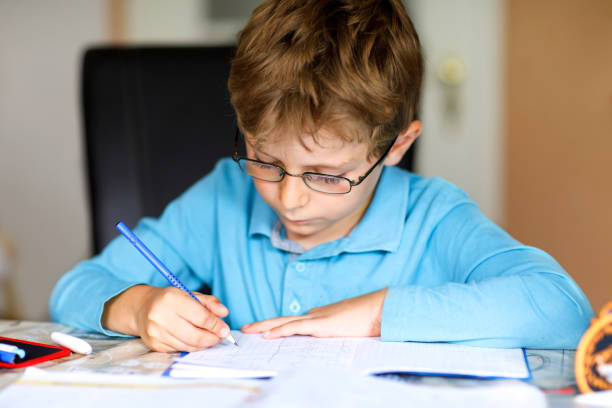 istock Cute little kid boy with glasses at home making homework, writing letters and doing maths with colorful pens. Little child doing exercise, indoors. Elementary school and education, imagine fantasy concept 1048066348