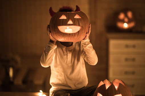 Small kid hiding his head with Jack O' Lantern on Halloween.