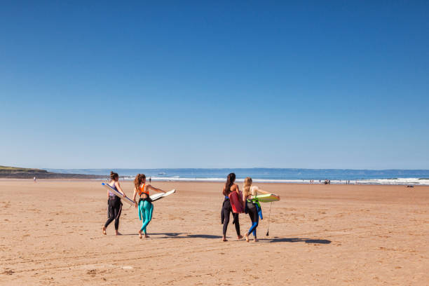 Women with Surfboards 18 June 2017: Croyde Bay, North Devon, England, UK - Four young women approch the sea with surf boards on one of the hottest days of the year. croyde bay photos stock pictures, royalty-free photos & images