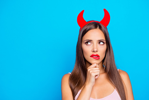 Portrait of confused puzzled unsure straight-haired caucasian girl wearing red horns, biting lip, isolated over bright vivid blue background, red pomade lips