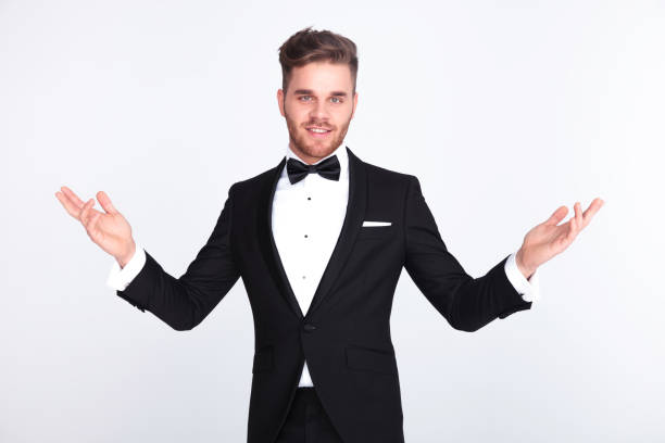 elegant man in tuxedo making a welcoming gesture elegant man in tuxedo making a welcoming gesture while standing on light grey background tuxedo stock pictures, royalty-free photos & images