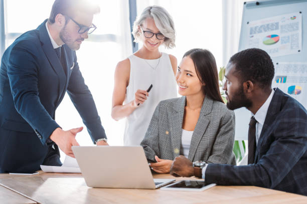 istock smiling multiethnic businesspeople working on project in office and looking at laptop 1048094744