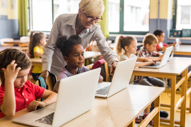 istock Happy mature teacher assisting school kids in using computers on a class. 1048099316