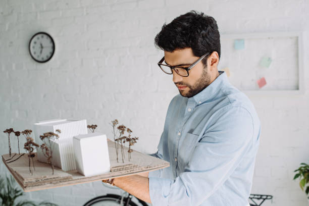 istock handsome architect in glasses looking at architecture model in office 1048100294