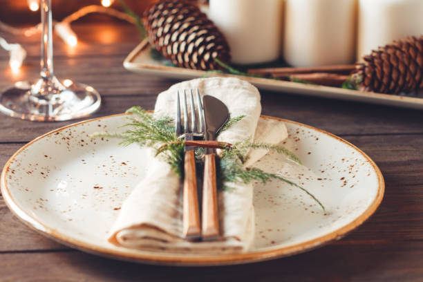 istock Thanksgiving table setting among white candles and cones. Ceramic plate with fork and knife on a linen napkin. The concept of a festive dinner. 1048103318