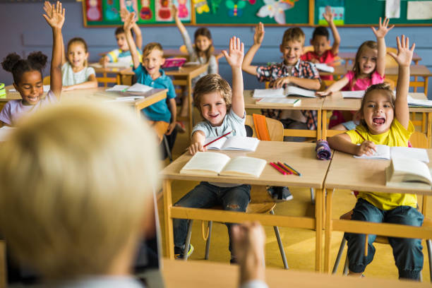 istock Large group of happy elementary students raising their hands to answer the question on a class. 1048104900