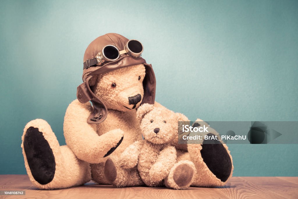 Retro Teddy Bear toy in leather pilot's hat and vintage goggles playing with baby front mint green wall background. Old style filtered photo Airplane Stock Photo