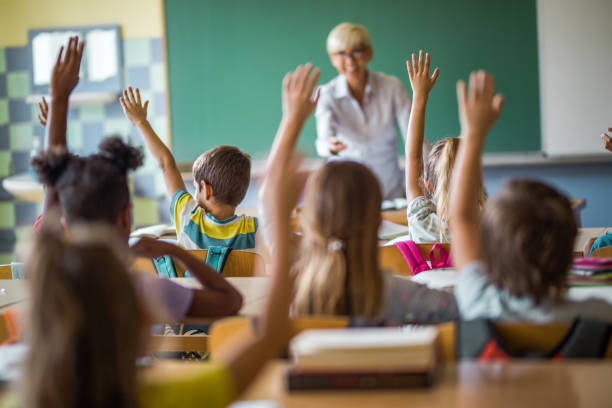 istock Rear view of elementary students raising arms on a class in the classroom. 1048109394