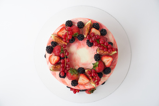 Cake with whipped pink cream, decorated with fresh strawberries, blackberry, figs and red currant on white background. Picture for a menu or a confectionery catalog. Top view.