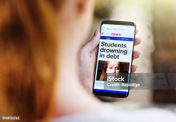 Students Drowning In Debt News Item On Mobile Phone Stock Photo - Download Image Now